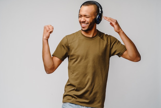 Happy african man smiling listening to music in headphones over grey wall