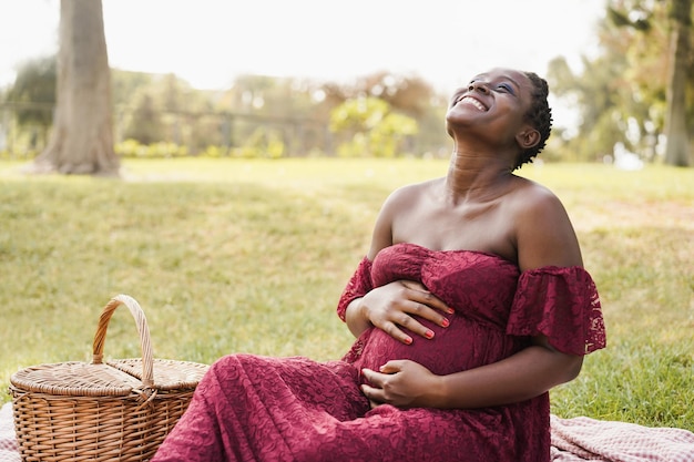 Happy african pregnant woman touching her belly outdoor at city park  Focus on face