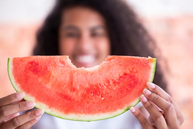 Happy african woman in the kitchen and holding slice of a watermelon  