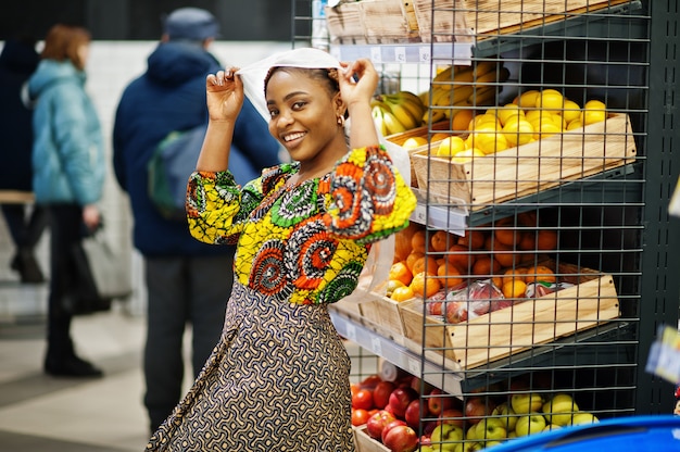 Happy african woman in traditional clothes and veil looking product at grocery store, shopping in supermarket.  Afro black  women costumer buying fruits at the market.