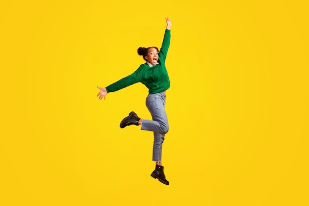 Happy afro girl jumps over yellow studio background