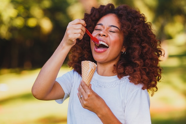 Happy afro woman eating ice cream in the park.