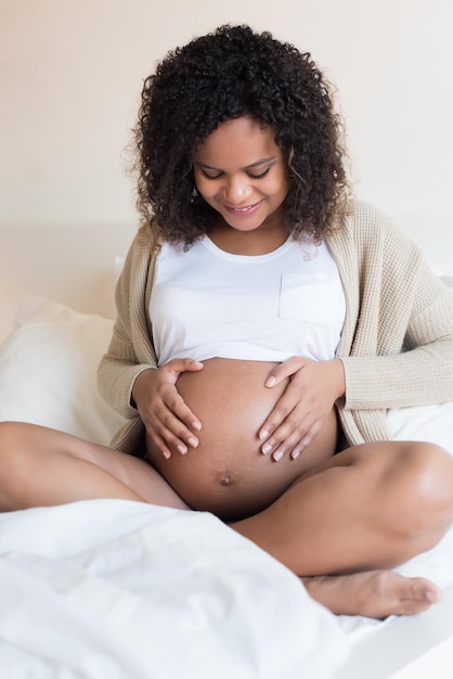 Happy afro woman showing her pregnant belly