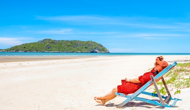 Happy alone woman relaxing on a wooden chair at a tropical beach enjoying the sea