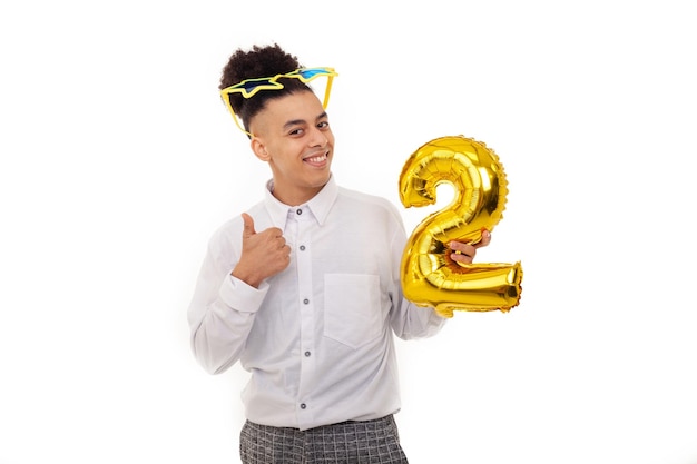 A happy American man with star glasses on head showing thumbs up holding a number two shaped balloon