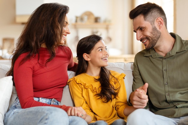 Happy arabic parents sitting with daughter on sofa at home