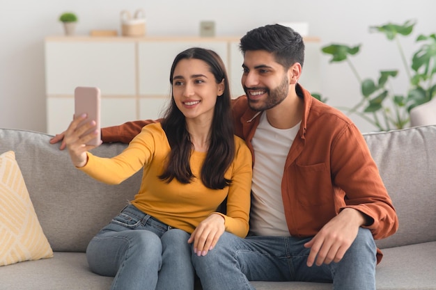 Happy arabic spouses making selfie using mobile phone indoor