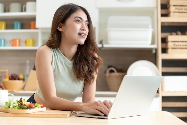 Happy Asia woman eating salad with see computer notebook in kitchen room