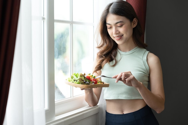 Happy Asia woman eating salad with sun light of window in living room