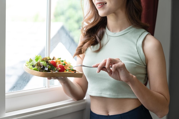 Happy Asia woman eating salad with sun light of window in living room