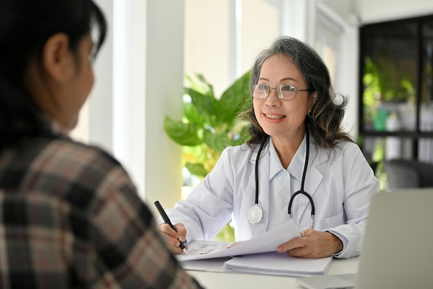 Happy Asian aged female doctor having a nice conversation with her patient in the clinic