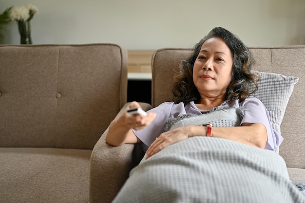 Happy Asian agedwoman enjoying her weekend leaning on the couch and watching TV show