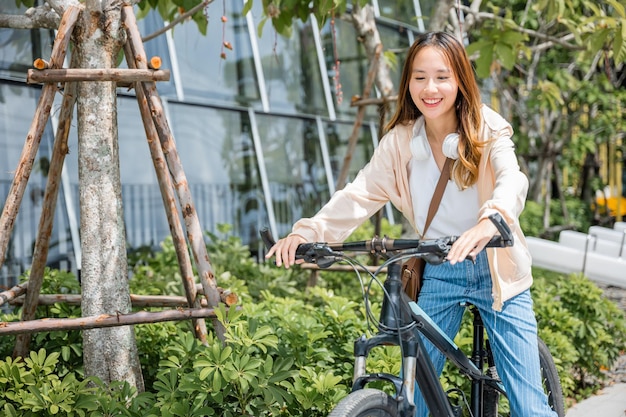 Happy Asian beautiful young woman riding bicycle on street outdoor near building city, Portrait of smiling female lifestyle using bike in summer travel means of transportation, ECO friendly