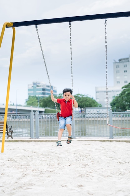 Happy asian boy swinging at the playground in the park