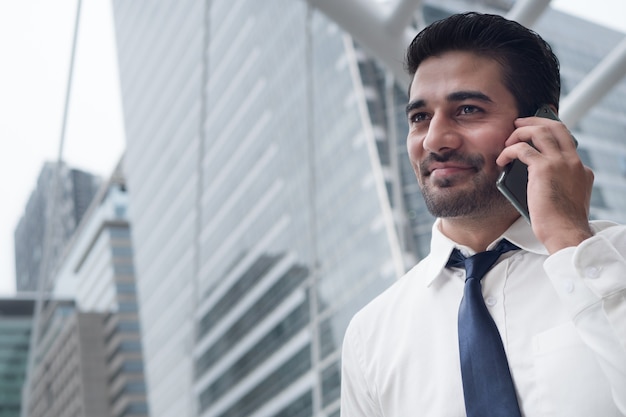 Happy asian business man talking smart phone; portrait of happy smiling successful Asian, Indian businessman talking via smart phone; negotiation, business deal, transaction, communication concept