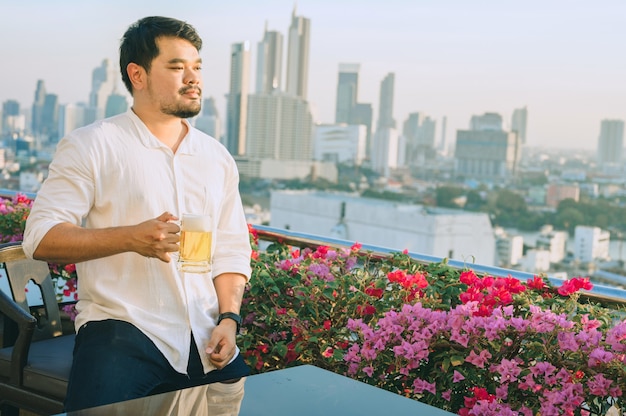 Happy asian businessman smiling while drinking beer at the rooftop restaurant