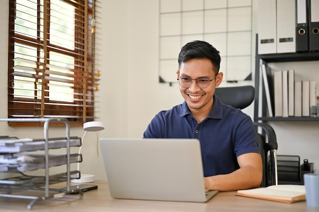 Happy Asian businessman working on his business project on laptop at his desk in the office