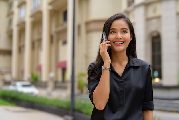 Happy Asian businesswoman outdoors in city street talking on phone while smiling and walking