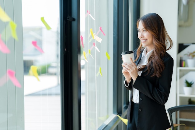 Happy Asian businesswoman in a suit holding a coffee cup Refreshing drink