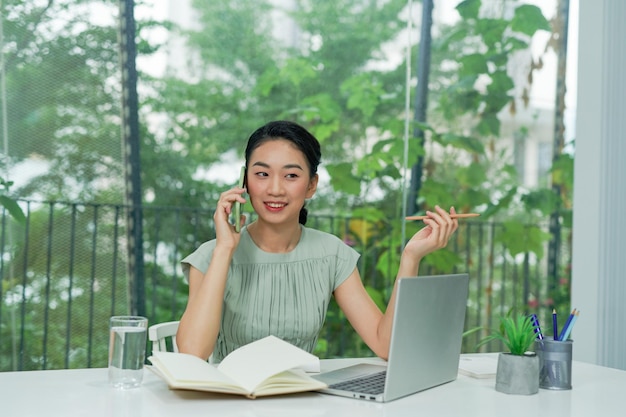 Happy Asian businesswoman talking on mobile at the office