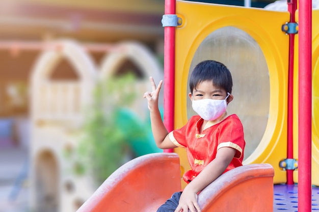 Happy Asian child boy smiling and wearing fabric mask, He playing with slider bar toy at the playground,