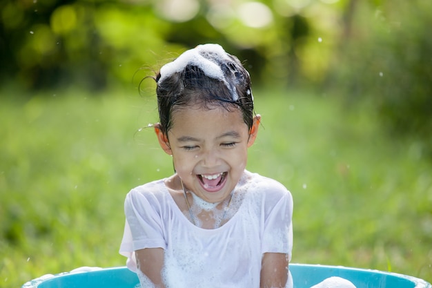 Happy asian child girl having fun to bath and play with foam in outside