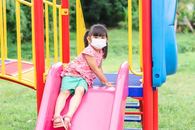 Happy Asian child girl smiling and wearing face mask She playing with toy at the playground