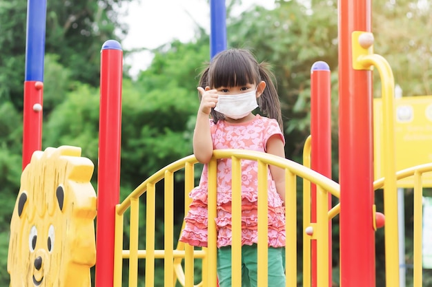 Happy Asian child girl smiling and wearing face mask She showing the thumb up fingers