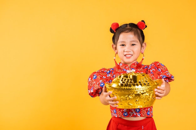 Happy Asian Chinese little girl smile wearing red cheongsam holding big gold ingot