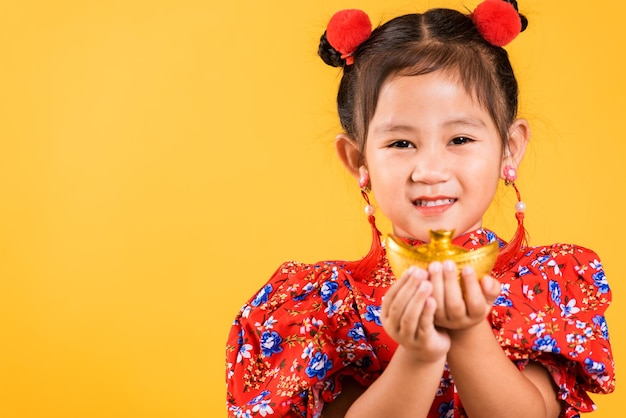 Happy Asian Chinese little girl smile wearing red cheongsam holding gold ingot