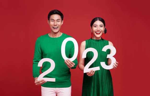 Happy asian couple in green casual attire showing number 2023 greeting happy new year