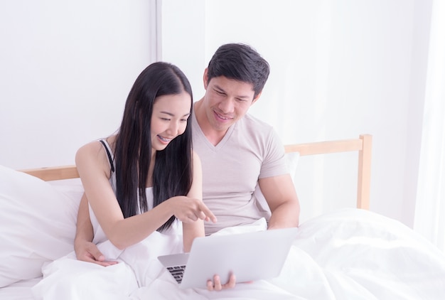 Happy Asian couple is using laptop on morning bed with smile