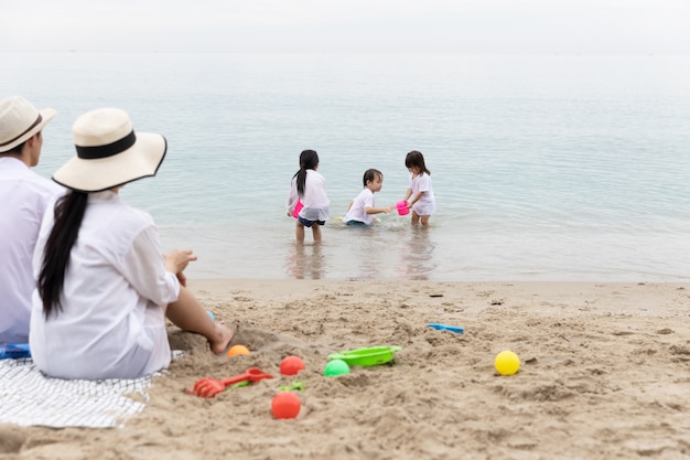 Happy Asian Family Brother and sister three playing toys on sand in the beach together In the morning time. Holiday and Travel concept.