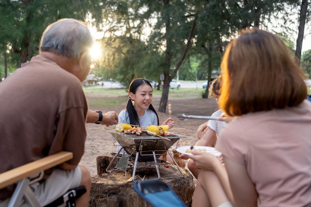 Happy Asian family having barbecue together. Cooking grilled bbq for dinner during camping on summer beach.