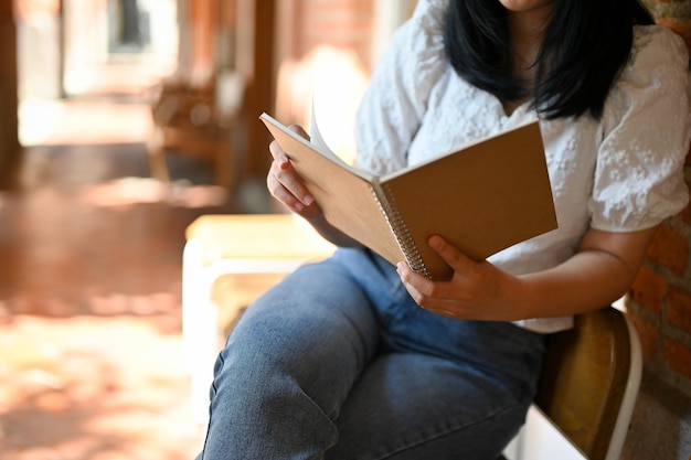 Happy Asian female enjoys reading a book while chilling at the city public square cropped image