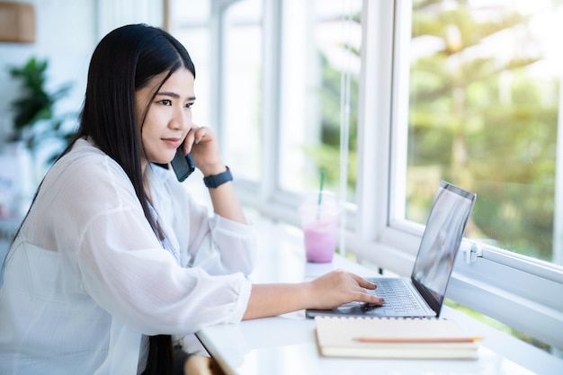 Happy of asian freelance people business female talking making using smartphone casual working with laptop computer with notebook for browsing internet chatting and blogging in a public coffee shop