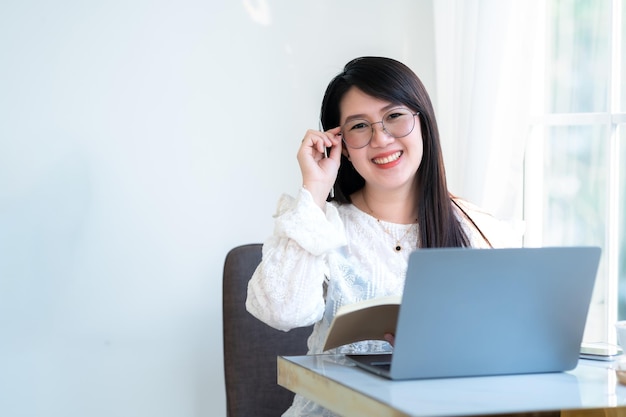 Happy of asian freelance people Businesswoman Taking written Notes to on notebook casual working with laptop computer with a coffee cup mug and smartphone at the cafeBusiness Lifestyle