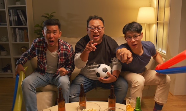 Happy asian friends or football fans watching soccer on tv and celebrating victory at home