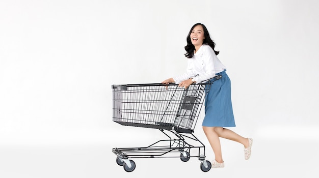 Happy asian girl with shopping cart on white isolated wall