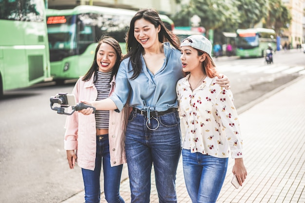 Happy asian girls making vlog video at bus station. Trendy friends blogging for social media outdoor