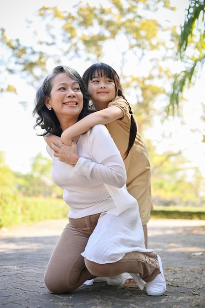 Happy Asian grandmother and her lovely granddaughter in the park piggy back