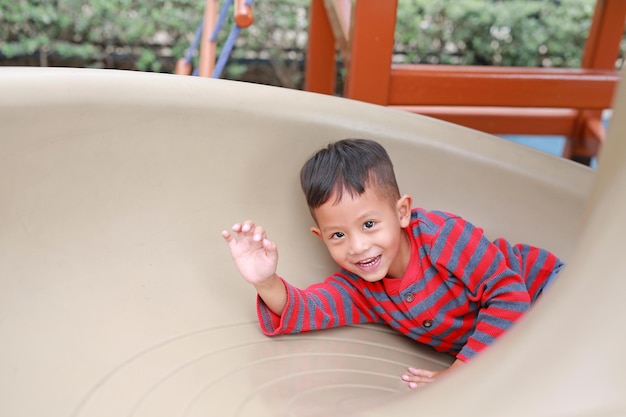 Happy Asian little boy having fun while playing slider in the playground