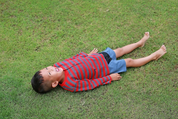 Happy Asian little boy lying down on green lawn Kid lies on grass looking on sky