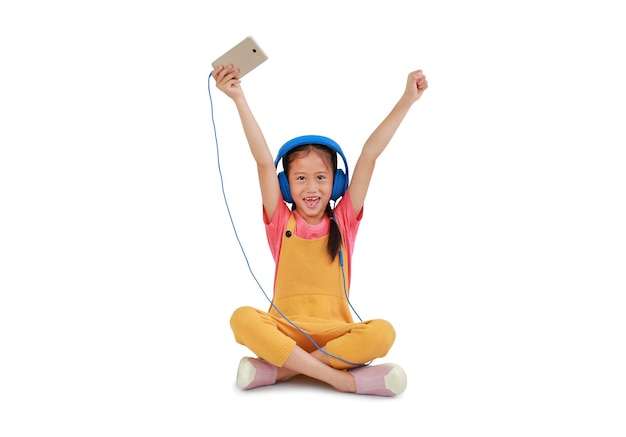 Happy Asian little girl child wearing headphones and enjoy with smartphone sitting isolated on white background Image with Clipping path