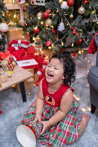 Happy Asian little girl have fun on Christmas day. Kid with parent with Christmas tree decoration at home on holiday.