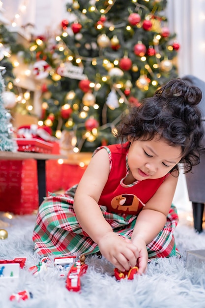 Happy Asian little girl have fun on Christmas day. Kid with parent with Christmas tree decoration at home on holiday.