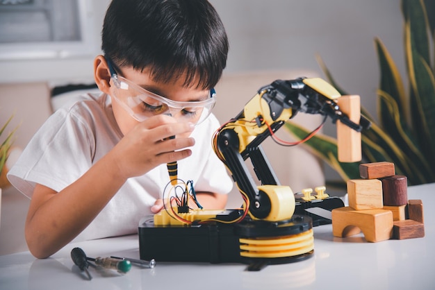 Happy Asian little kid boy using screwdriver to fixes screws robotic machine arm in home workshop