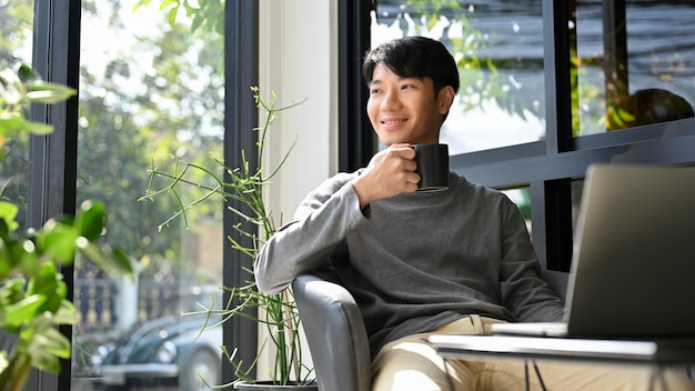 Happy Asian male enjoys having coffee at the coffee shop daydreaming about his career success