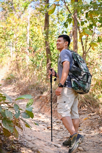 Happy Asian male traveler with trekking gear and backpack enjoys trekking in the forest alone