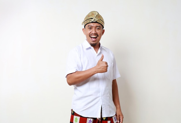 Photo happy asian man in balinese traditional costume standing while showing thumbs up isolated on white background